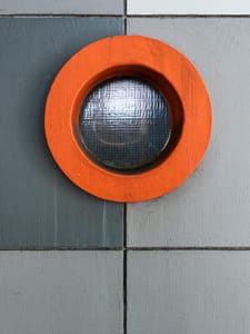 An orange light on a gray wall in the street.